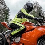 A motorcycle rider in retroreflective rain gear sits on a red Ducati Panagale sport bike